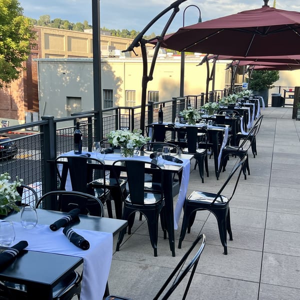 Outdoor rooftop dining area with black tables, white runners, floral centerpieces, and red umbrellas.