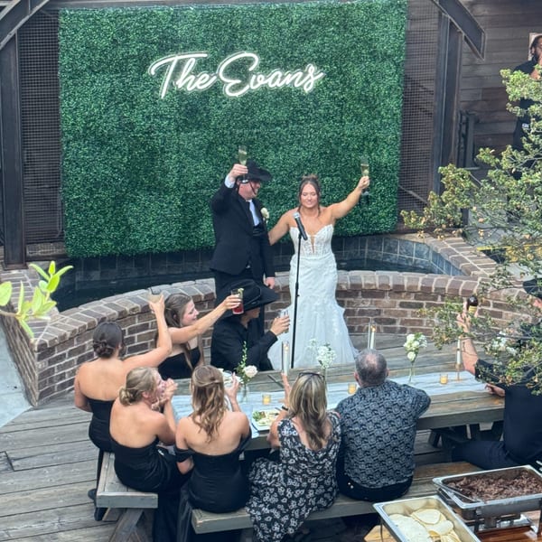 A wedding reception with a couple toasting in front of a green wall with "The Evans" in neon.