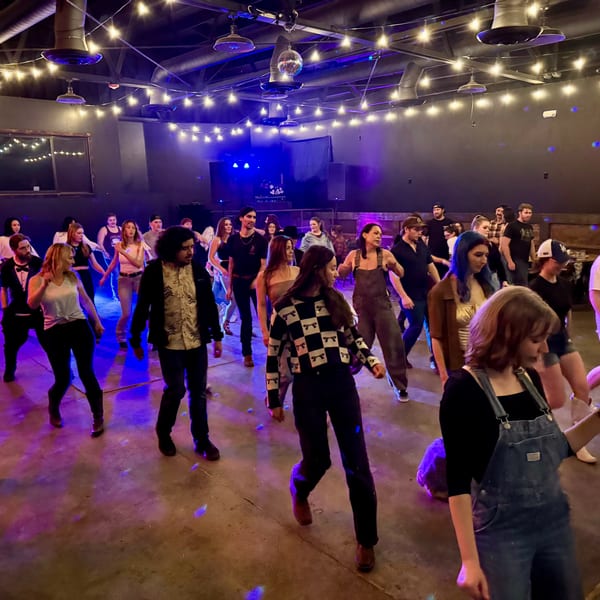 People dancing on a dimly lit dance floor with string lights and blue and purple lighting.