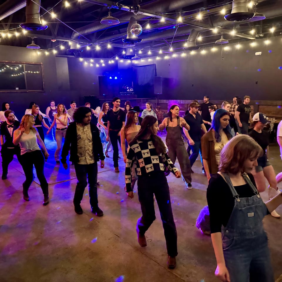 People dancing on a dimly lit dance floor with string lights and blue and purple lighting.