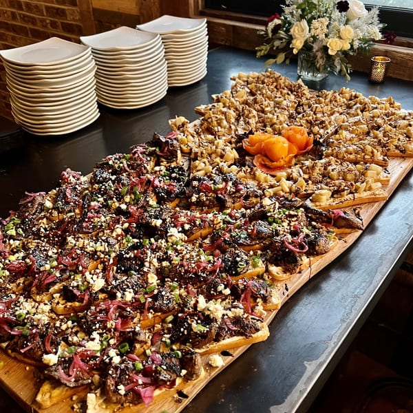 A long wooden board filled with appetizers, including bruschetta and fruit tarts, on a dark counter.