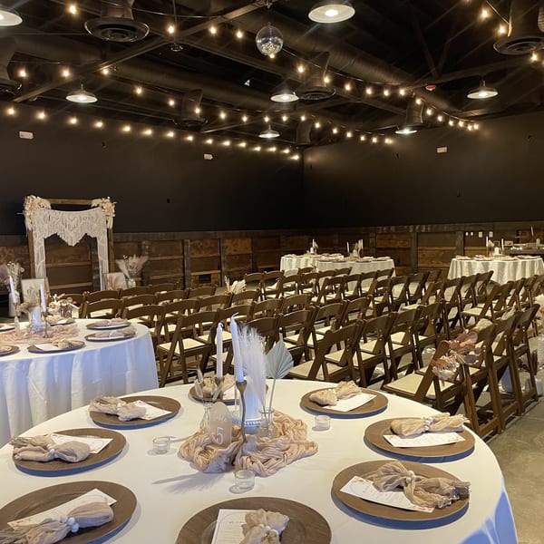 A large event space set up for a wedding with round tables, chairs, and string lights.
