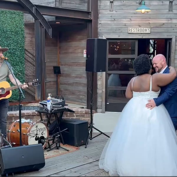 A musician plays guitar for a dancing couple at an outdoor event with a neon sign.