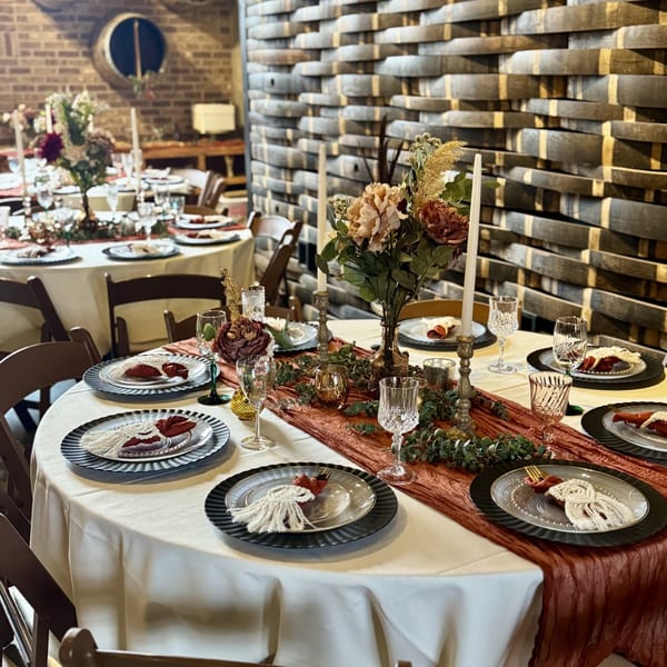 Elegant dining tables set with floral centerpieces, candles, and place settings in a rustic room.