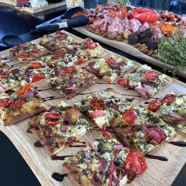 Flatbread slices with tomatoes, prosciutto, and cheese, next to charcuterie and cheese boards.