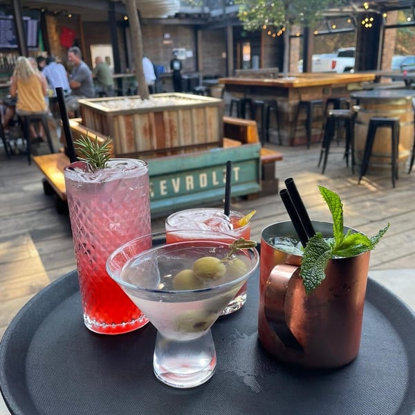 A tray of cocktails, including a martini and Moscow mule, on an outdoor patio with people.