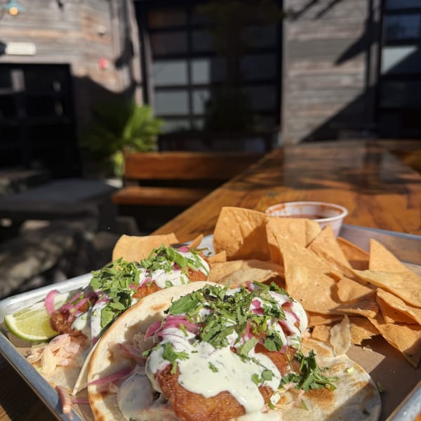 Two fish tacos with cilantro, pickled onions, and sauce, alongside tortilla chips and salsa.