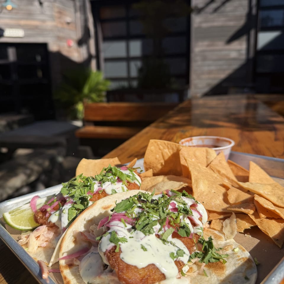 Two fish tacos with cilantro, pickled onions, and sauce, alongside tortilla chips and salsa.