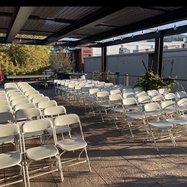 Rows of white folding chairs arranged under a covered outdoor patio for an event.