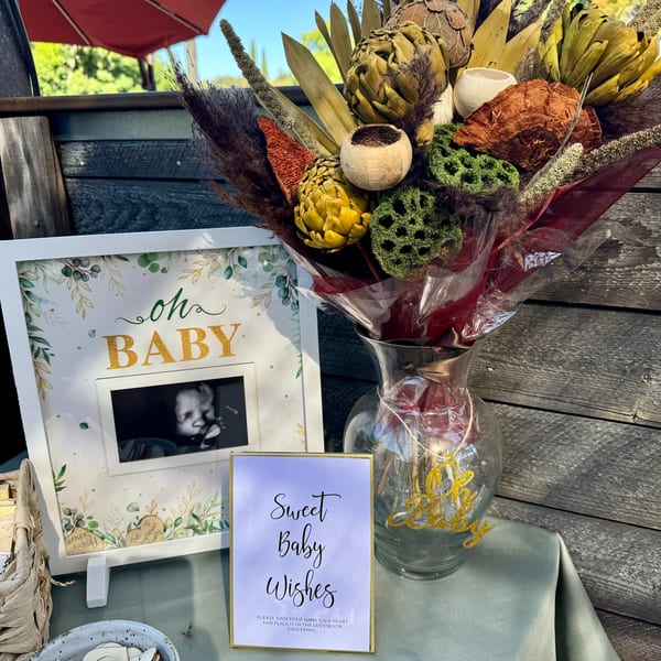 A baby shower display with a sonogram photo, a "Sweet Baby Wishes" sign, and a dried floral arrangement.