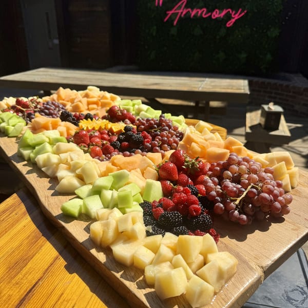 A large wooden board filled with various cut fruits, including melon, grapes, strawberries, and berries, on an outdoor table.