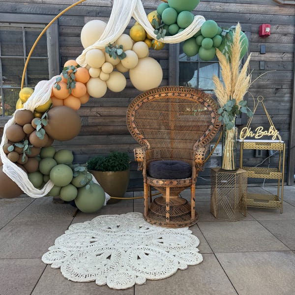 A peacock chair, balloon arch, and "Oh Baby" sign create a baby shower photo backdrop.
