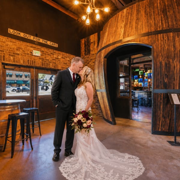 A bride and groom kiss in a rustic-industrial space with a large wooden barrel entrance.