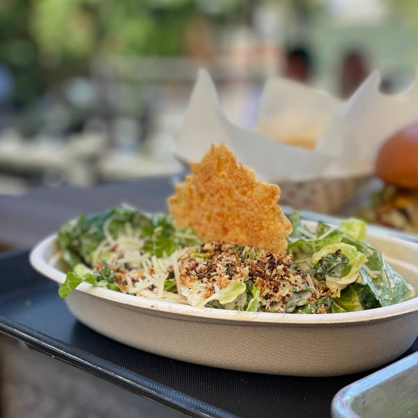 Caesar salad with parmesan crisp and toasted nuts in a white bowl on a black tray.