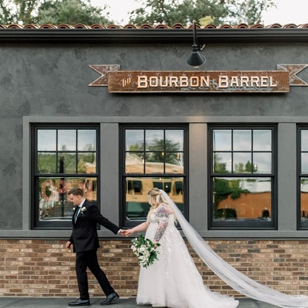 A newlywed couple walks hand-in-hand in front of The Bourbon Barrel restaurant.