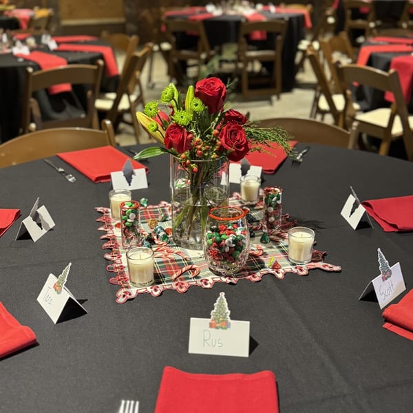 A festive holiday table setting with red roses, candles, and candy on a black tablecloth.
