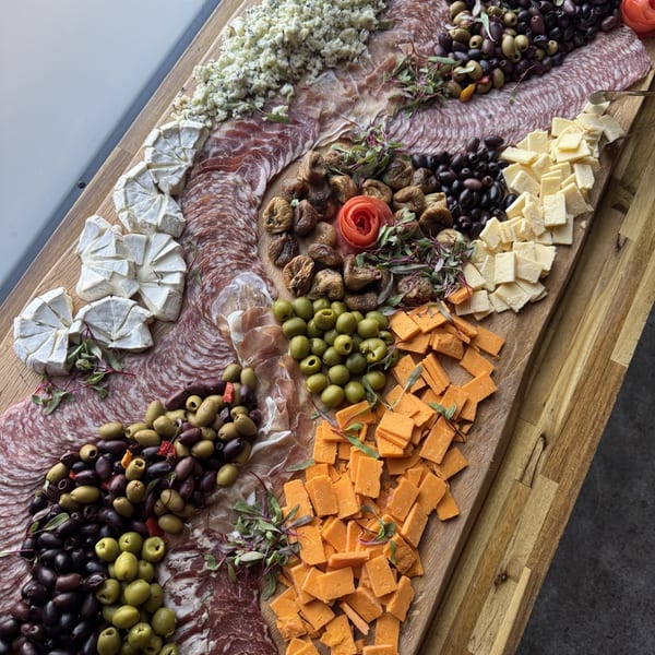 A large wooden charcuterie board filled with various cheeses, cured meats, olives, and dried figs.