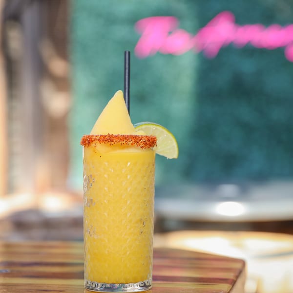A vibrant yellow frozen drink with a chili-lime rim and a lime wedge on a wooden table.