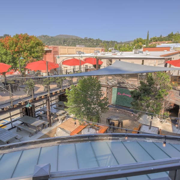 Overhead view of a multi-level outdoor patio with red umbrellas, picnic tables, and string lights.